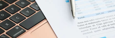 Financial documents and pen are on laptop keyboard