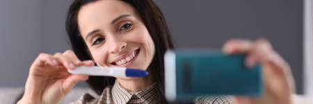 Smiling woman shows pregnancy test in smartphone