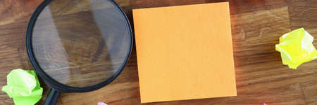 Many crumpled multicolored stickers and magnifying glass lying on wooden tableの写真素材