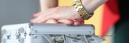 Female hands closing metal suitcase with dollar bills closeup