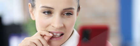 Young woman biting her nails looking at phone screen