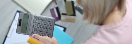Woman holding calculator in hands and writing in notebook closeupの写真素材