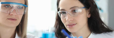 Two scientists with glasses look at test tube of liquid.