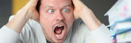 Dumbfounded man holds his head and looks at the stack of folders