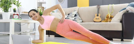 Woman makes side plank and looks into laptop monitor