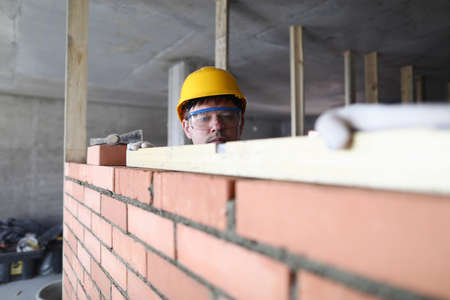 Portrait of builder laying bricks using special tools. Worker building brick wallsの写真素材