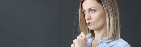 Pensive businesswoman holds pen and looks into distanceの写真素材