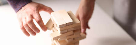 Several hands reach for wooden blocks from the toy tower