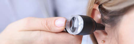 Otorhinolaryngologist looking at patients ear using an otoscope closeup