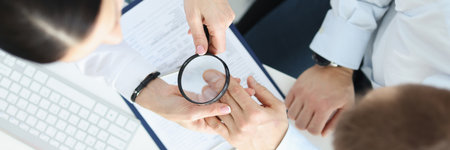 Dermatologist looking at patients skin on hands with magnifying glass top view