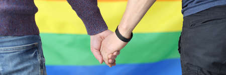 Young men holding hands with lgbt flag background closeupの写真素材