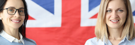 Two smiling women stand with notebooks in front of British flagの写真素材