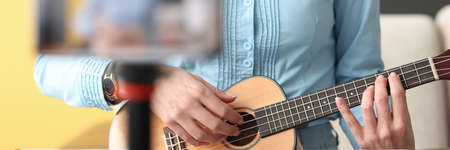 Woman playing ukulele and filming phone closeup