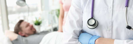 Doctor standing with his arms crossing on background of sick patientの写真素材