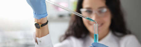 Woman chemist dripping blue liquid into test tube closeupの写真素材