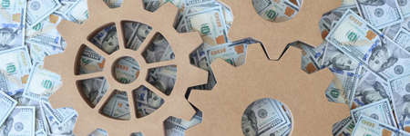 Wooden gears lying on lot of dollar billsの写真素材