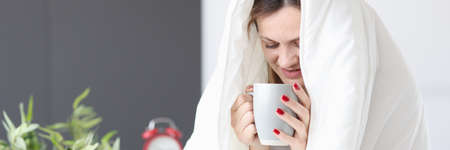 Woman sitting in bed under covers and drinking teaの写真素材