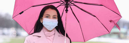 Woman in protective medical mask standing under umbrella