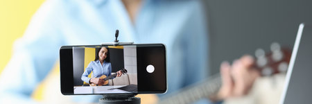 Woman is recording video on smartphone playing guitarの写真素材