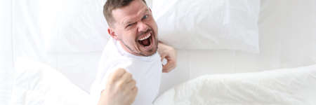 Young man lying in bed and rejoicing top view