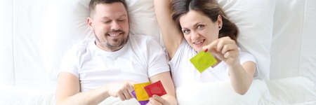 Man and woman lying in bed and holding condoms top view