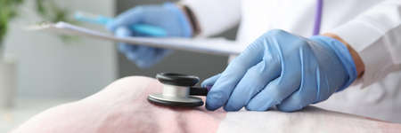 Doctor in protective gloves listening to patients heartbeat with stethoscope closeup