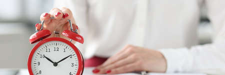 Woman sitting at table with book and clicking on alarm clock closeupの写真素材