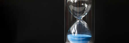 Stylish glass hourglass with blue sand close up
