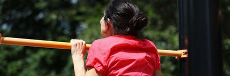 Woman in shirt pulls herself up on horizontal barの写真素材