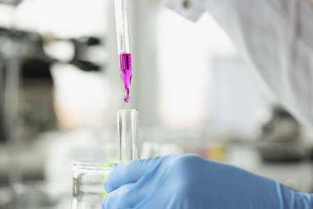 Scientist drops purple liquid from pipette into test tube
