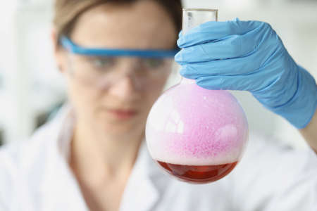 Woman scientist holding flask with purple liquid with foam in laboratory