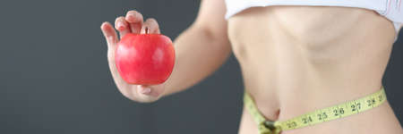 Woman with measuring tape at waist holding apple in hands closeupの写真素材