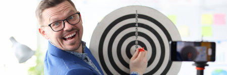 Businessman playing darts in front of mobile phone cameraの写真素材