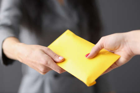 Woman hands yellow closed envelope with money to employeeの写真素材