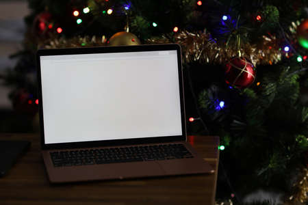 Laptop with blank white screen on behind is Christmas tree with garland