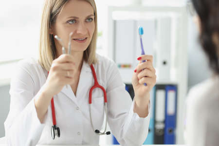 Woman doctor dentist shows patient toothbrush and dental instrument