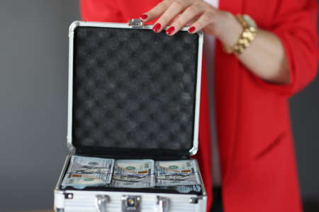 Woman in business suit holds suitcase full of money closeup