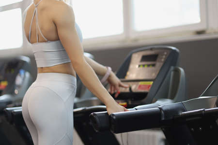 Athletic girl turns on treadmill for training closeup