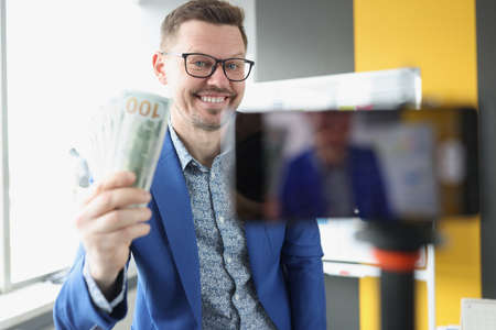 Smiling blogger demonstrates cash one hundred dollar bills to camera