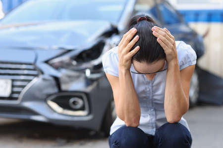 Frightened woman sits in front of wrecked car closeupの写真素材