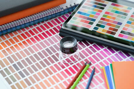 Magnifying glass lying on paper with color samples near digital tablet closeupの写真素材