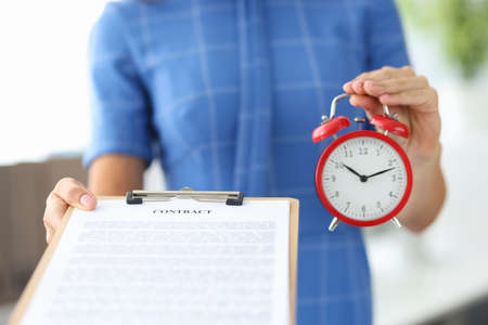 Woman holding contract and red alarm clock in her hands closeupの写真素材