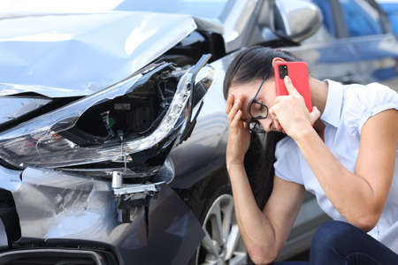 Sad woman talking on cell phone near broken car