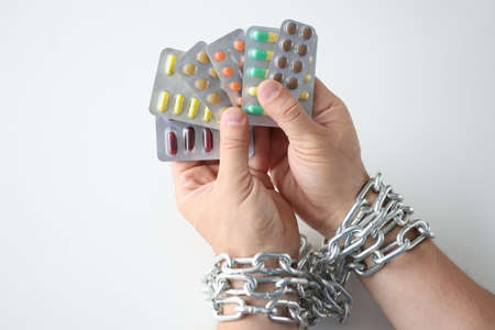 Male hands tied with chain and hold various medical pills closeup