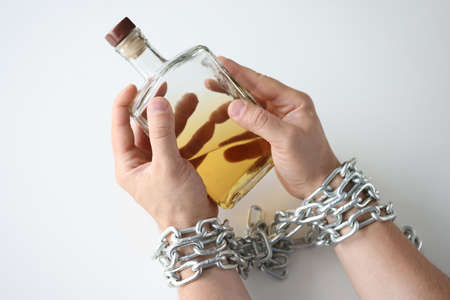 Male hands tied with chain and hold bottle of alcohol closeupの写真素材