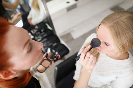 Woman in salon applies powder to blonde with brushの写真素材