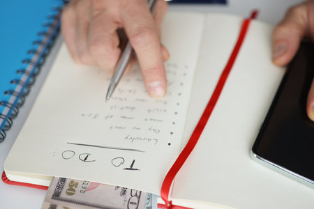 Man holding notepad with to-do list for today near mobile phone closeup