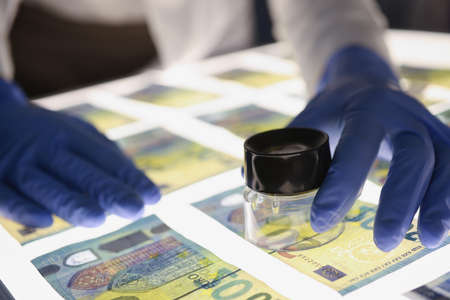 Man in rubber gloves checking authenticity of euro bills using lens closeupの写真素材