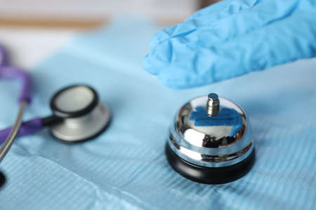 Hand in rubber medical gloves pressing bell near stethoscope closeup