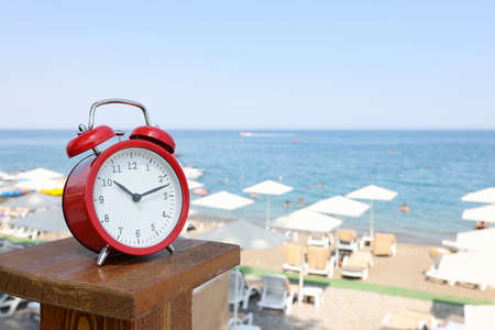 Red alarm clock standing on sea beach of hotel closeupの写真素材